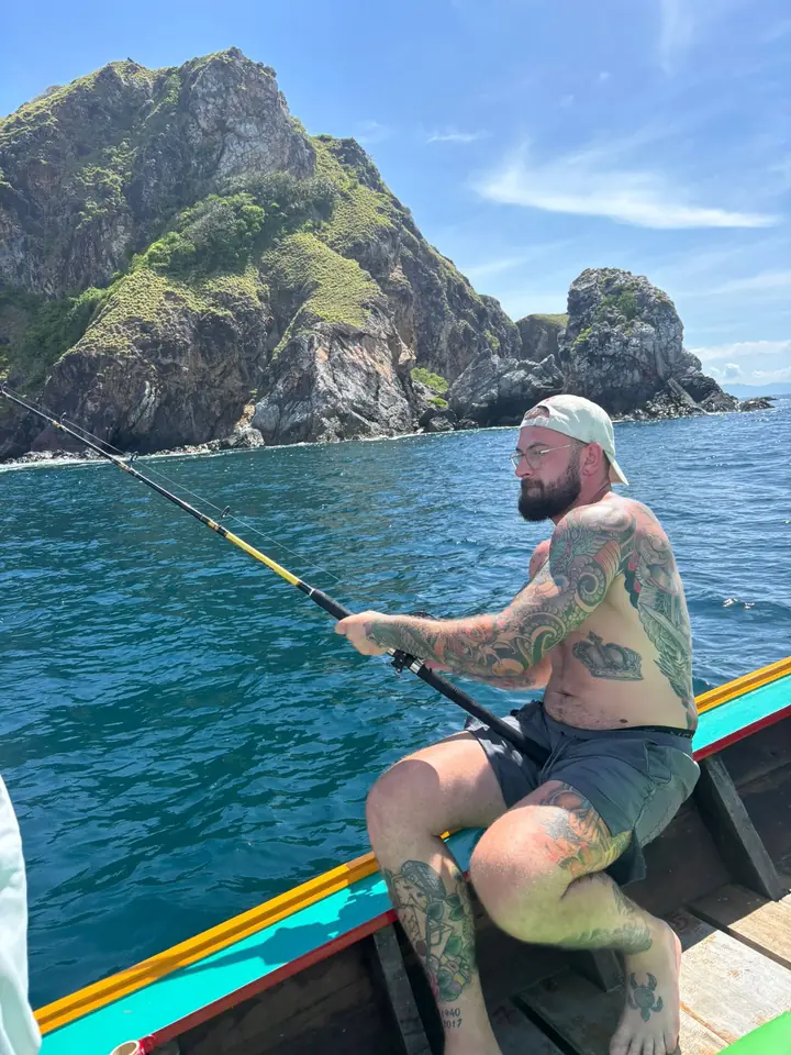 Guest fighting a fish with a rod from a longtail beside a limestone island in the Andaman Sea
