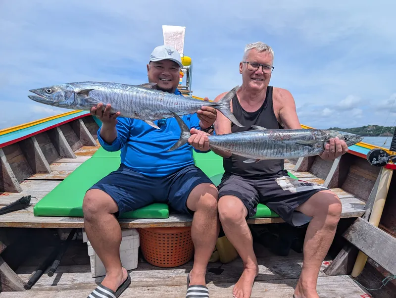 Two anglers sitting on a longtail, each holding a king mackerel